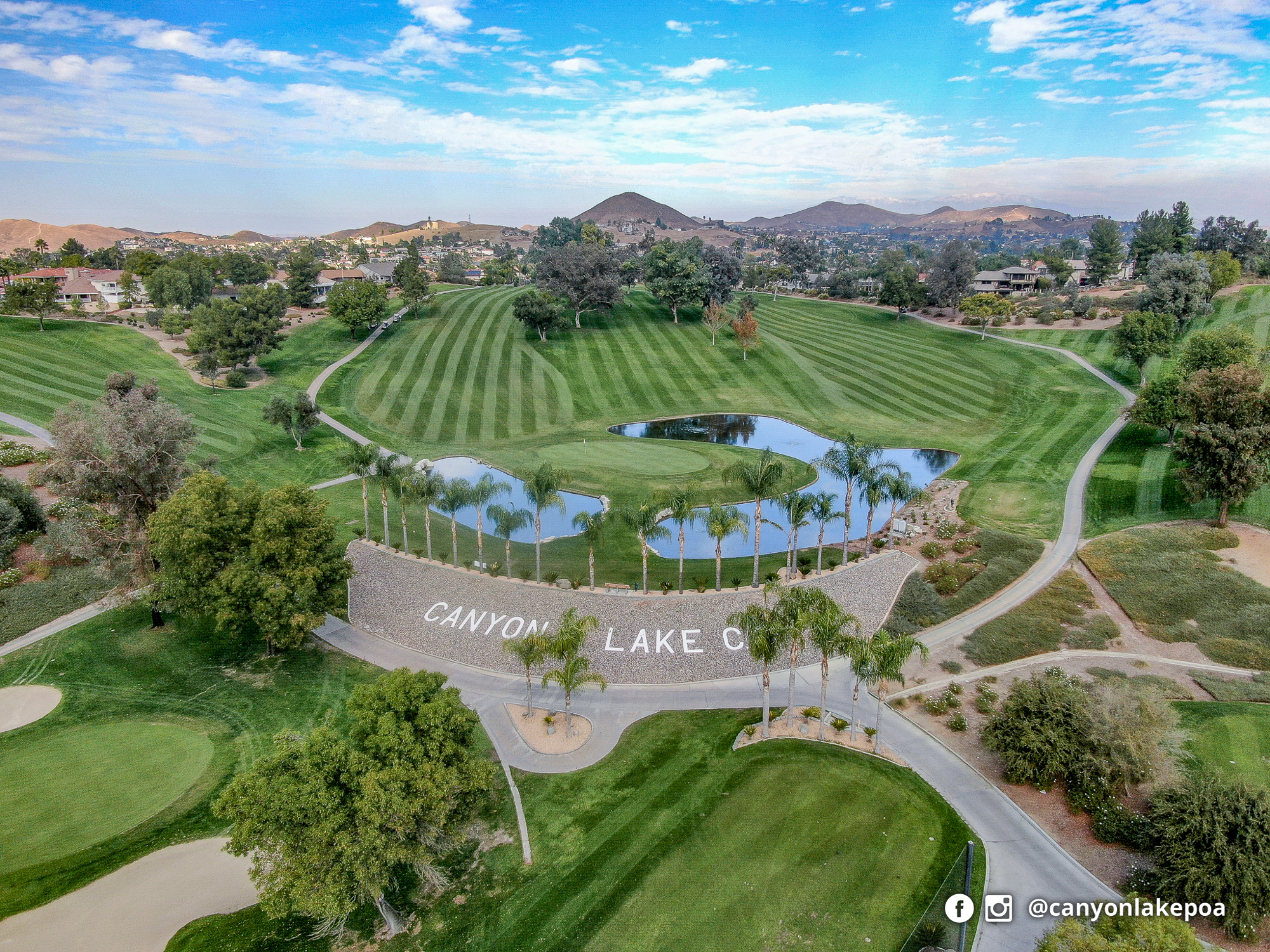 Aerial view of Canyon Lake’s golf course, with striped fairways, a water-lined green, palms and surrounding hills.