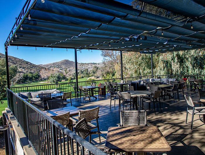 Covered patio at the Canyon Lake Country Club Bar & Grill, with dining tables overlooking the golf course and surrounding hills.